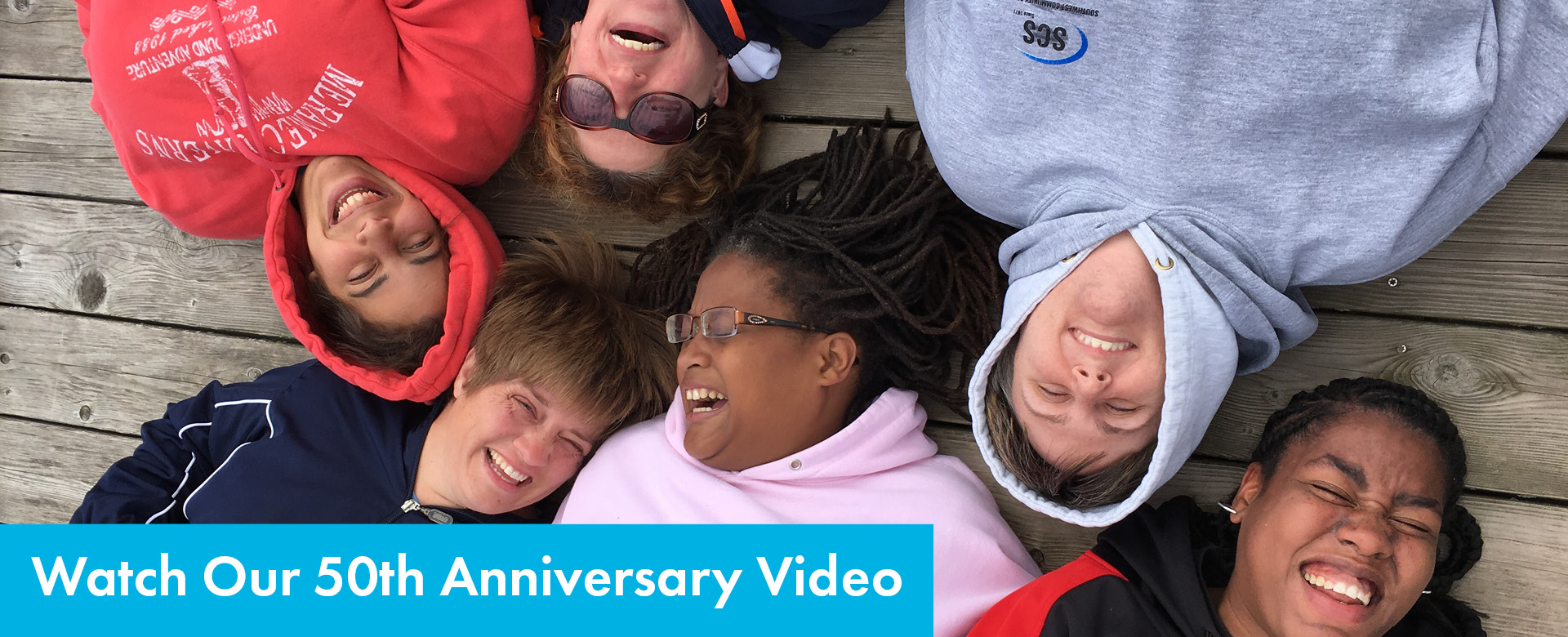 Overhead shot of 6 SSSRA participants laying on deck, laughing together. Text: Watch Our 50th Anniversary Video
