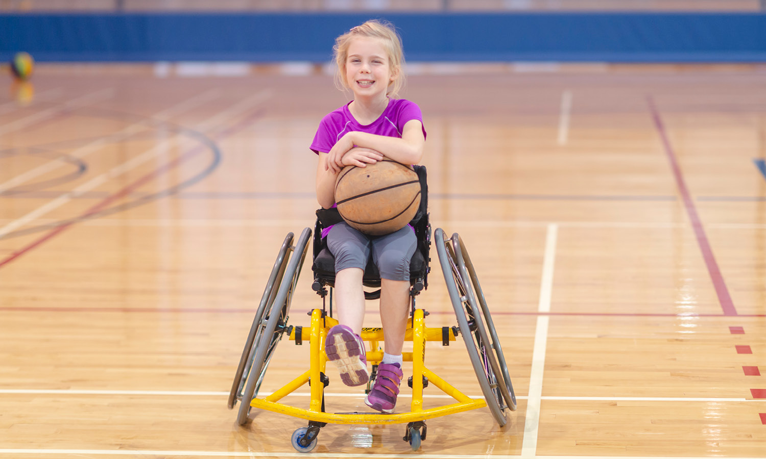 Young girl in wheelchair holding basketball on the basketball court.