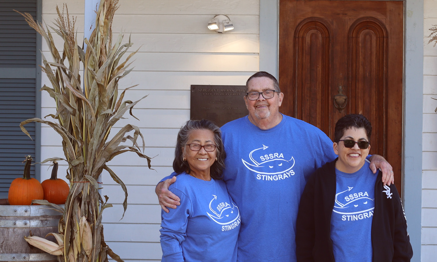 Family poses on the porch at the Bradford Barn. Pumpkins and cornstalks decorate the porch.